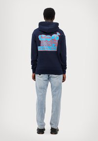 Hanorac navy cu un imprimeu grafic pe spate, prezentând desene cu înghețată în nuanțe de roz și albastru. Sweatshirt-ul are o croială lejeră și o buzunar tip kangaroo.
