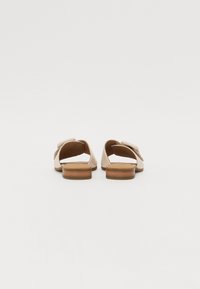 Sandali aperti beige chiaro con tacco a blocco in legno di dimensioni ridotte, caratterizzati da una design a fasce incrociate e una texture morbida.