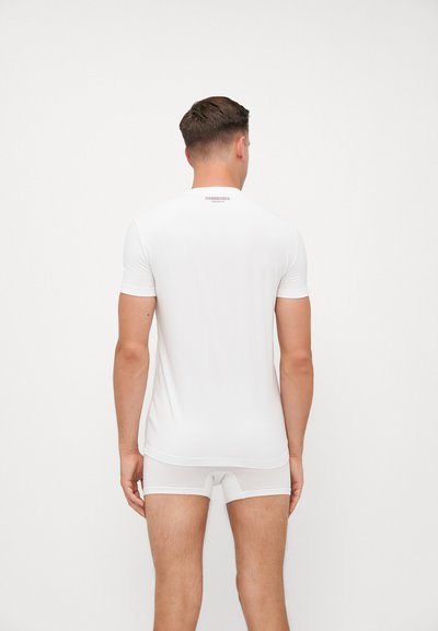 Weißes, tailliertes Kurzarmhemd aus glattem Stoff, kombiniert mit weißen Unterhosen. Minimale Markenkennzeichnung im oberen Rückenbereich. Sauberes, schlichtes Design.
