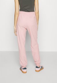 Light pink, elastic waistband sweatpants with side pockets, tapered leg design, paired with pink and navy sneakers featuring tan soles.