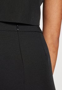 Svart jumpsuit med en figursydd overdel och textilstruktur. Sidofickor synliga, med en liten dragkedja i midjan.