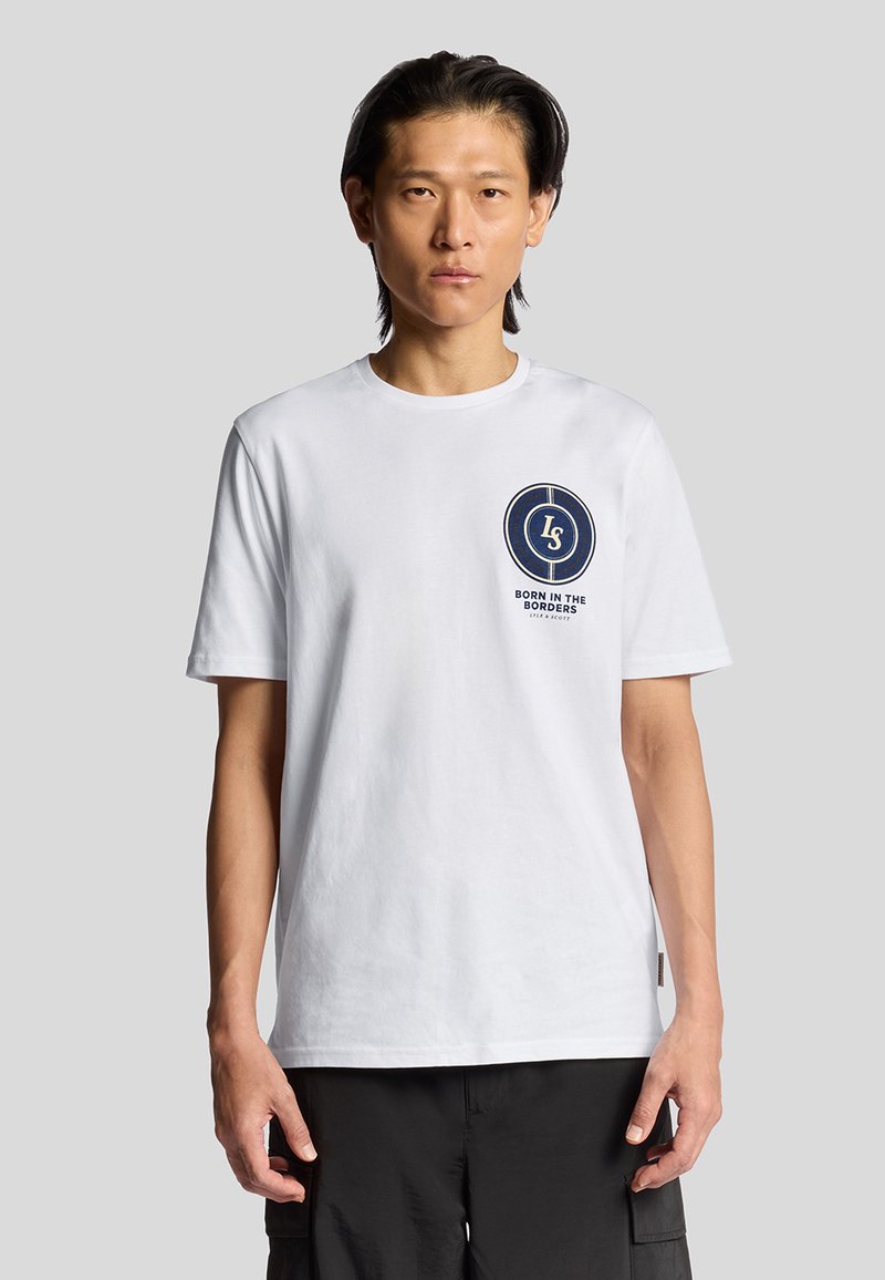 Hvid bomulds-t-shirt med et cirkulært marineblåt logo med teksten "LS" og "BORN IN THE BORDERS", korte ærmer og rund halsudskæring.