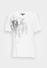 Camiseta blanca de manga corta hecha de una tela suave, con un diseño gráfico en gris desgastado de letras en la parte frontal. Cuello redondo.