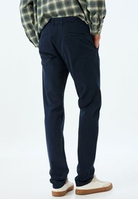 Mörkblå byxor i mjukt tyg med rak bendesign, två bakfickor och kombinerade med vita sneakers.