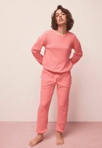 Ružová bavlnená mikina a zodpovedajúce nohavice s voľným strihom, dlhými rukávmi, elastickým pásom a bočnými vreckami. Hladká textúra.