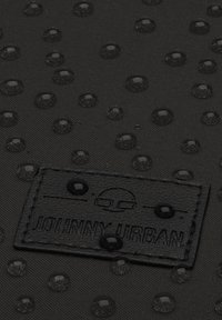 Fekete vízálló szövet, emelt körszerű mintákkal és a "JOHNNY URBAN" feliratú textúrált címkével. Sima, tartós textúra fényes részletekkel.