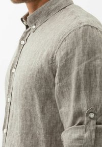 Helles graues Leinenhemd mit Button-Down-Kragen, ausgestattet mit weißen Knöpfen und hochgerollten Ärmeldetails. Weicher, strukturierter Stoff mit lockerer Passform.