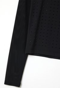 Schwarzes Langarmshirt aus strukturiertem Material mit einem Netzpaneel und dekorativen schwarzen Perlenakzenten, die in einem gepunkteten Muster angeordnet sind.