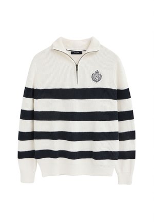 Jersey blanco de punto con rayas horizontales negras, cuello con cremallera hasta media altura y un pequeño escudo bordado en el pecho izquierdo.