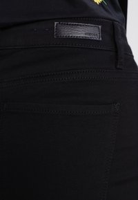 Zwarte denim jeans met een gladde textuur, een leren label op de tailleband en gestikte details rond de zakken.