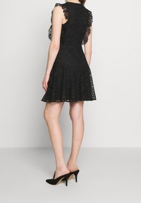 Musta pitsimekko, jossa on tiukka yläosa, levenevä helma ja röyhelöhiha. Yhdistetty mustiin mokkanahkakenkiin, joissa on terävät kärjet ja ohuet korot.