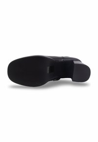 Vue de la semelle d'une chaussure en cuir noir avec un talon carré et une semelle extérieure lisse et plate sur fond blanc.