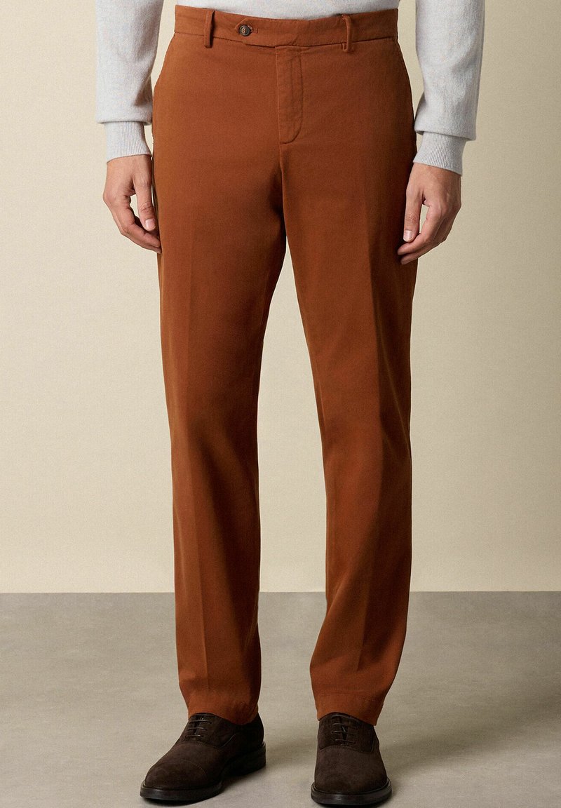 Braune Baumwollhosen mit flacher Vorderseite, Reißverschluss und einem einzelnen Knopf, ausgestattet mit Seitentaschen und einer taillierten Passform.