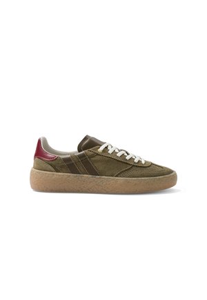 Baskets basses en daim vert olive avec lacets blancs, détails en cuir marron, languette de talon rouge et semelle extérieure en gomme texturée.