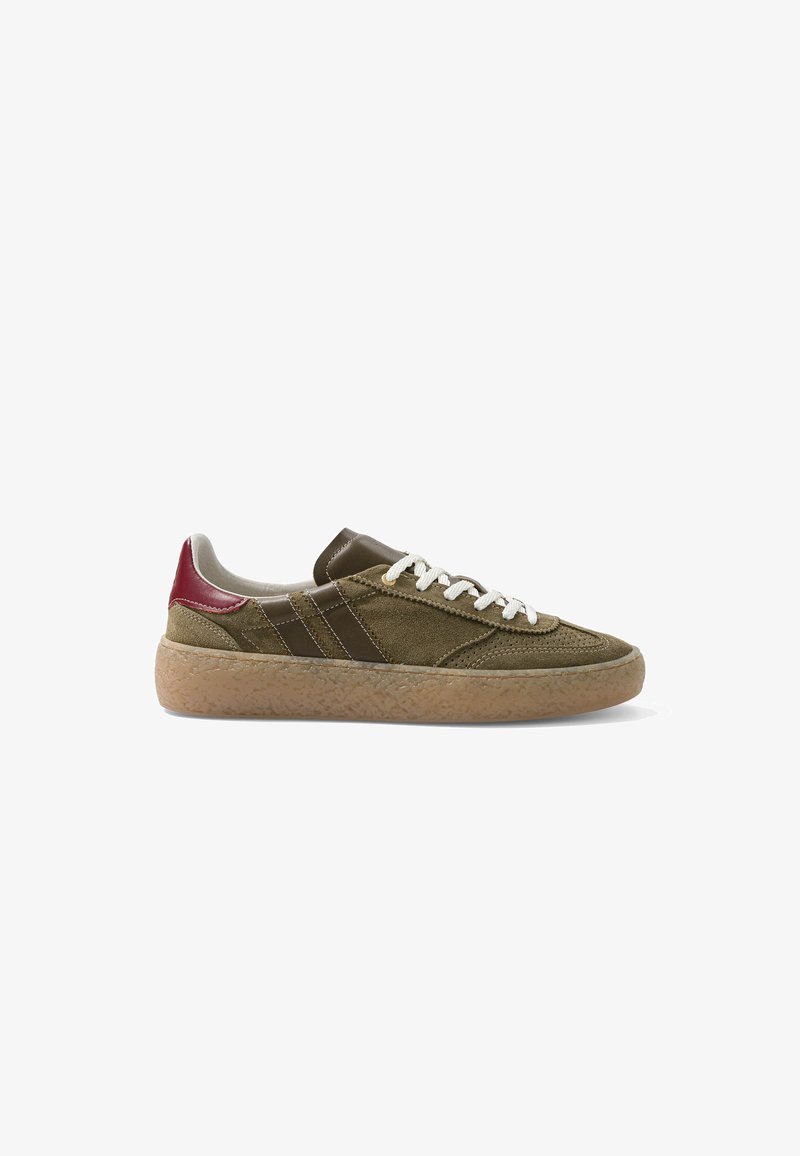 Baskets basses en daim vert olive avec lacets blancs, détails en cuir marron, languette de talon rouge et semelle extérieure en gomme texturée.