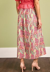 Lunga gonna rosa con motivi floreali e foglie, fascia elastica in vita e silhouette fluida. Abbinata a scarpe con tacco alto rosa chiaro.