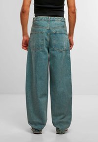 Lyseblå vide jeans med høy midje, to baklommer og glatt tekstur, vist bakfra mot en nøytral bakgrunn.