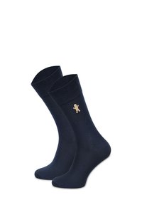 Granatowe bawełniane skarpety z prążkowanym ściągaczem, z małym beżowym emblematem piernikowego ludzika z boku. Gładka faktura i długość do połowy łydki.