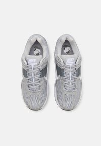 Šedé Nike tenisky s síťovaným vrškem, kontrastními šedými akcenty a bílými detaily. Mají kulatou špičku a texturovanou podrážku.