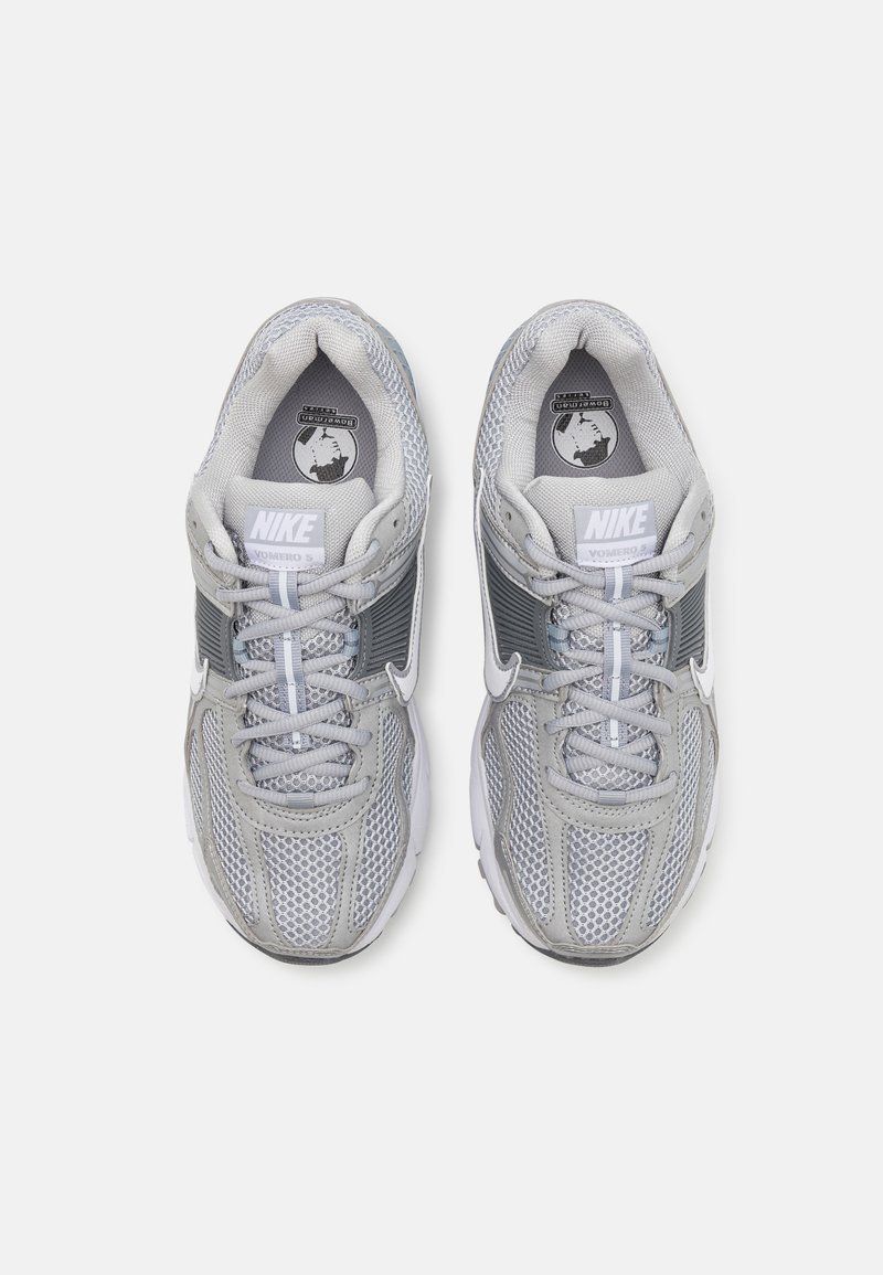 Zapatillas Nike grises con parte superior de malla, acentos grises contrastantes y detalles en blanco. Presenta una puntera redonda y una suela texturizada.