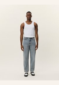 Light blue denim jeans with a straight-leg design, featuring a zipper fly, five pockets, and a subtle faded finish. Paired with a white tank top.