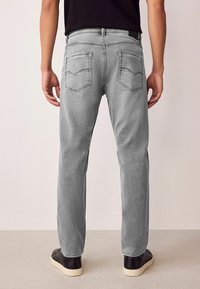 Blugi gri din denim cu croială cu picior drept, având două buzunare în spate cu cusături în formă de V și o finisare ușor texturată a țesăturii.