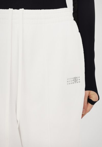 White jogger pants made of soft fabric, featuring an elastic waistband, drawstring, and a small printed graphic with numbers on the side.