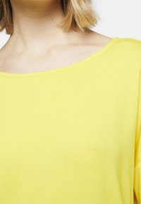 Žluté oversized tričko s širokým výstřihem a krátkými rukávy. Vyrobeno z hladkého, lehkého materiálu s pevným povrchem.