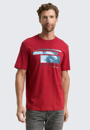 Rotes Baumwoll-T-Shirt mit kurzen Ärmeln, ausgestattet mit einem blauen grafischen Design und Text auf der Vorderseite. Rundhalsausschnitt und gerader Saum.