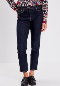 Donkerdenim jeans met een slim fit, voorzien van contrasterende stiksels, een knoopsluiting en voorkruiszakken. Gepaard met glanzende zwarte instappers.