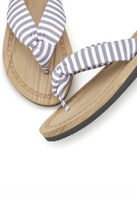 Gestreepte teenslippers met stoffen bandjes in grijs en wit op een houten binnenzool, met een gestructureerde zwarte rubberen zool en decoratieve rand.