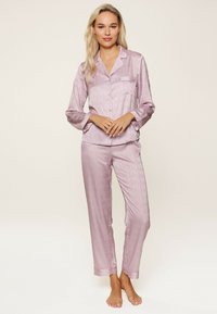 Satin-Pyjamas in hellem Lavendel mit einem dezenten Logomuster. Das Set umfasst ein Hemd mit Knopfleiste und gerade geschnittene Hosen, die auf Komfort ausgelegt sind.