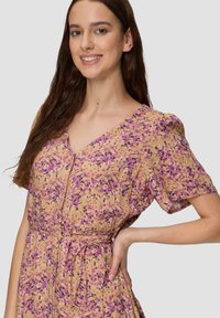Blumenmusterkleid in Hellgelb mit lila Punkten, kurzen Puffärmelchen, einem V-Ausschnitt und einer taillierten Schnürung. Leichtes Gewebe.