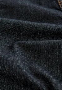 Tamsiai mėlynos džinsinės medžiagos audinys rodo smulkų, tekstūruotą audinį su subtiliais sidabriniais taškais, sulankstytas, kad išryškėtų lygus, vienodas paviršius ir švelnus blizgesys.