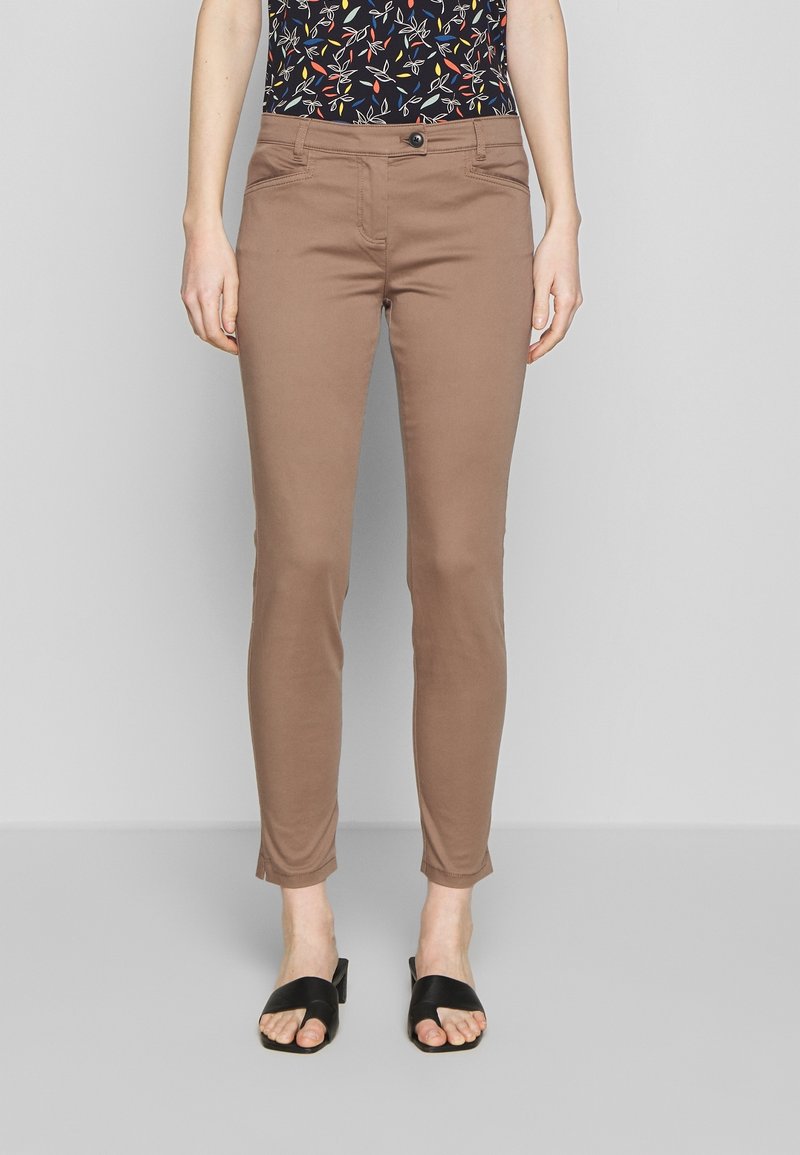 Bruine slimfit broek met een soepele textuur, voorzien van een ritssluiting en knoopsluiting. Gecombineerd met zwarte open teen schoenen.