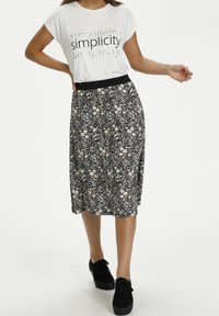 T-shirt blanc avec le texte "simplicité" en noir, associé à une jupe noire à fleurs avec de petites marguerites et une taille élastique noire. Chaussures noires.