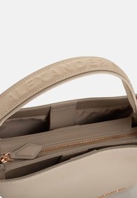 Borsa a mano in pelle color beige chiaro con manico superiore, logo impresso sulla tracolla e scomparto con zip dotato di zip color oro.