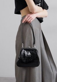 Black crocodile-embossed handbag with a structured shape, silver hardware, and a short handle, held by an individual in gray attire.