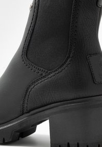 Černé kotníkové boty s hladkou kůží a elastickými textilními panely, s robustním podpatkem a dekorativním prošíváním pro zvýšení detailu.