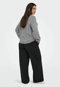 Grijze oversized trui met geribbelde onderrand en mouwen, gecombineerd met wijde zwarte broek. Soepele textuur, casual pasvorm.