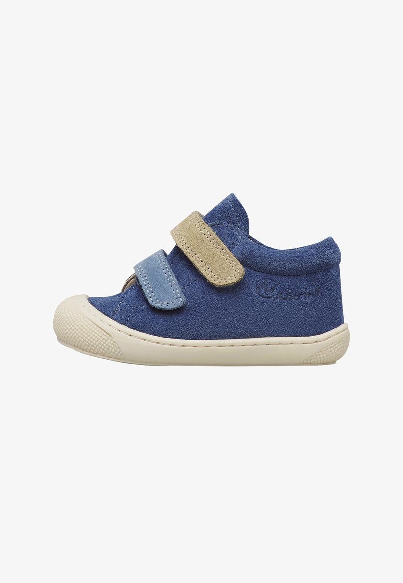 Blauwe suède peutersneaker met beige en blauwe klittenbandsluitingen en witte rubberen zool, zijaanzicht op witte achtergrond.