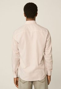 Chemise à boutons avec des rayures verticales roses et blanches, manches longues et col classique. Tissu en coton lisse et ourlet arrondi.