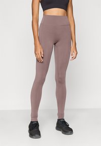 Κολάν με ψηλή μέση και εφαρμοστή γραμμή από ύφασμα μαύρου χρώματος με ομαλή υφή. Διαθέτει επίπεδες ραφές και συνδυάζεται με μαύρα αθλητικά παπούτσια.