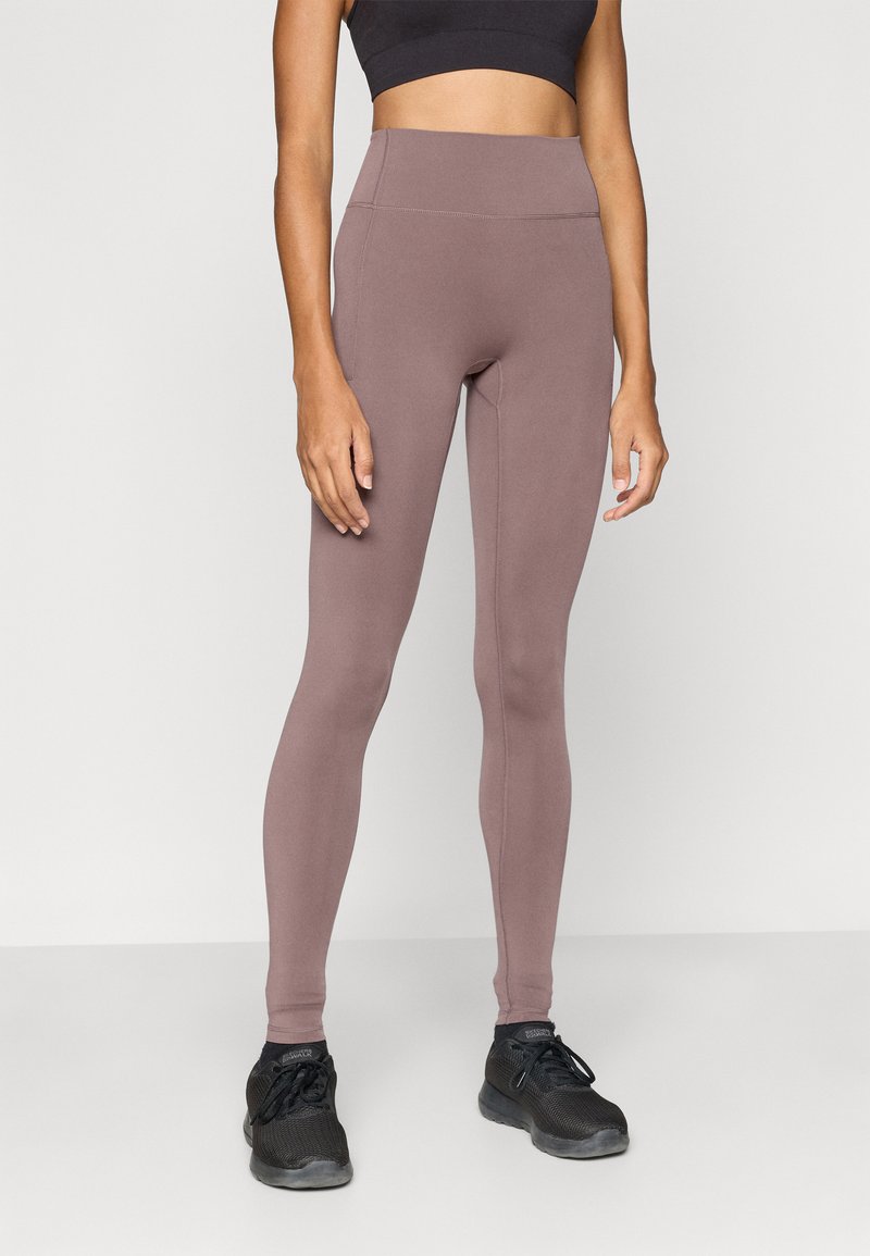 Κολάν με ψηλή μέση και εφαρμοστή γραμμή από ύφασμα μαύρου χρώματος με ομαλή υφή. Διαθέτει επίπεδες ραφές και συνδυάζεται με μαύρα αθλητικά παπούτσια.