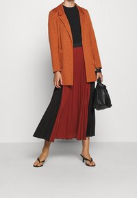 Orange blazer over a black top, paired with a pleated skirt in red and black. Accessories include a black handbag and black flip-flops.