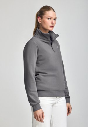 Grijze zip-up sweatshirt met hoge kraag, geribde manchetten en zoom, gemaakt van zachte stof, met een klein logo op de borst, gedragen met witte broek.