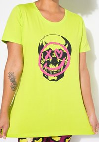 T-shirt vert fluo avec un graphisme de crâne noir entouré de rose et exprimant des émotions, confectionné en tissu doux, à manches courtes et avec un col arrondi.