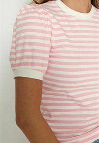 Rozā un baltā svītru īsām piedurknēm blūze ar ribotu tekstūru, ar baltu apaļu kakla izgriezumu un pūkainām piedurknēm.