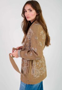Cardigan marron clair avec un motif cachemire en crème et bleu. Doté d'une ceinture à nouer et de poignets côtelés. Fabriqué en matériau tricoté doux.