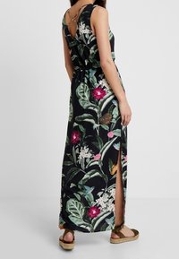 Vestido largo con estampado floral sobre un fondo negro con flores rosas y blancas. Tiene cintura ceñida, aberturas y tirantes cruzados en la espalda.